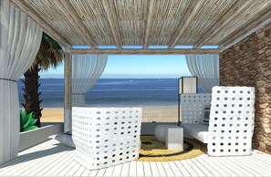 A covered outdoor seating area with a view of the ocean, featuring white furniture and a stone wall. - Byblos Mare (Thasos)