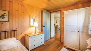 Ein Zimmer mit Holzwänden, einem Bett, einem Schminktisch mit Spiegel und Lampe sowie einem Kleiderschrank.