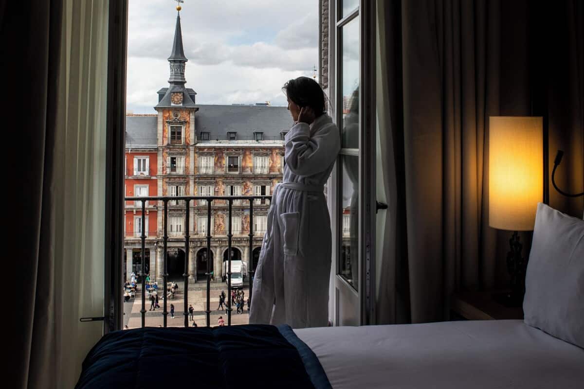 Une chambre d’hôtel avec une grande fenêtre, un lit, une lampe de chevet et une vue sur un immeuble doté d’une tour.
