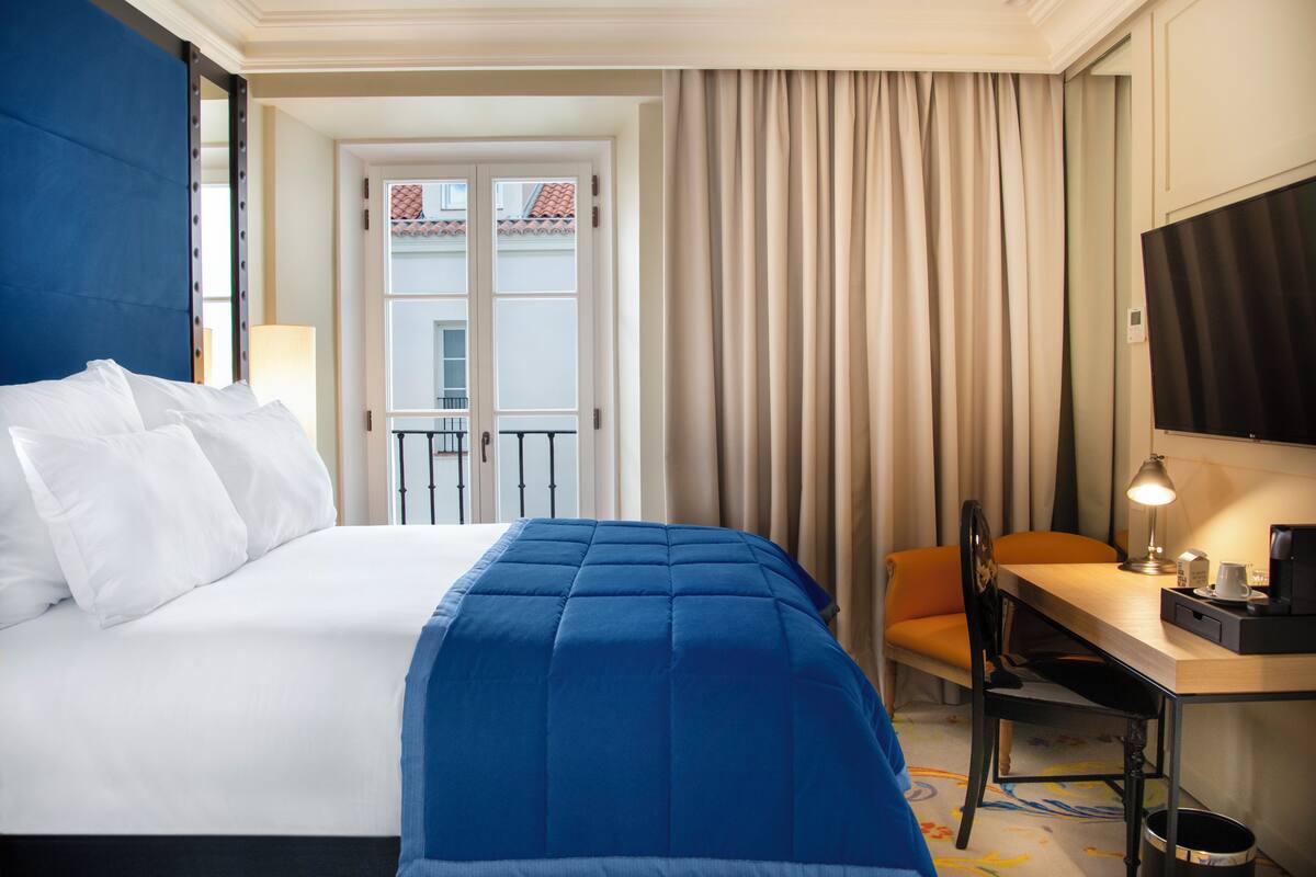 Une chambre d’hôtel avec un lit, un bureau, une chaise, une télévision et une fenêtre avec des rideaux.