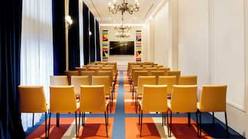 Un salón de conferencias con filas de sillas amarillas, una pantalla grande y una araña.