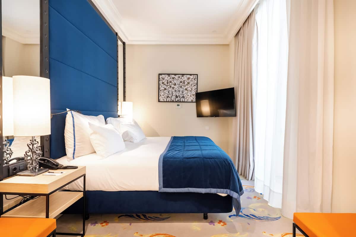 Une chambre d’hôtel avec un lit, un bureau doté d’une lampe, un téléphone et un téléviseur fixé au mur.