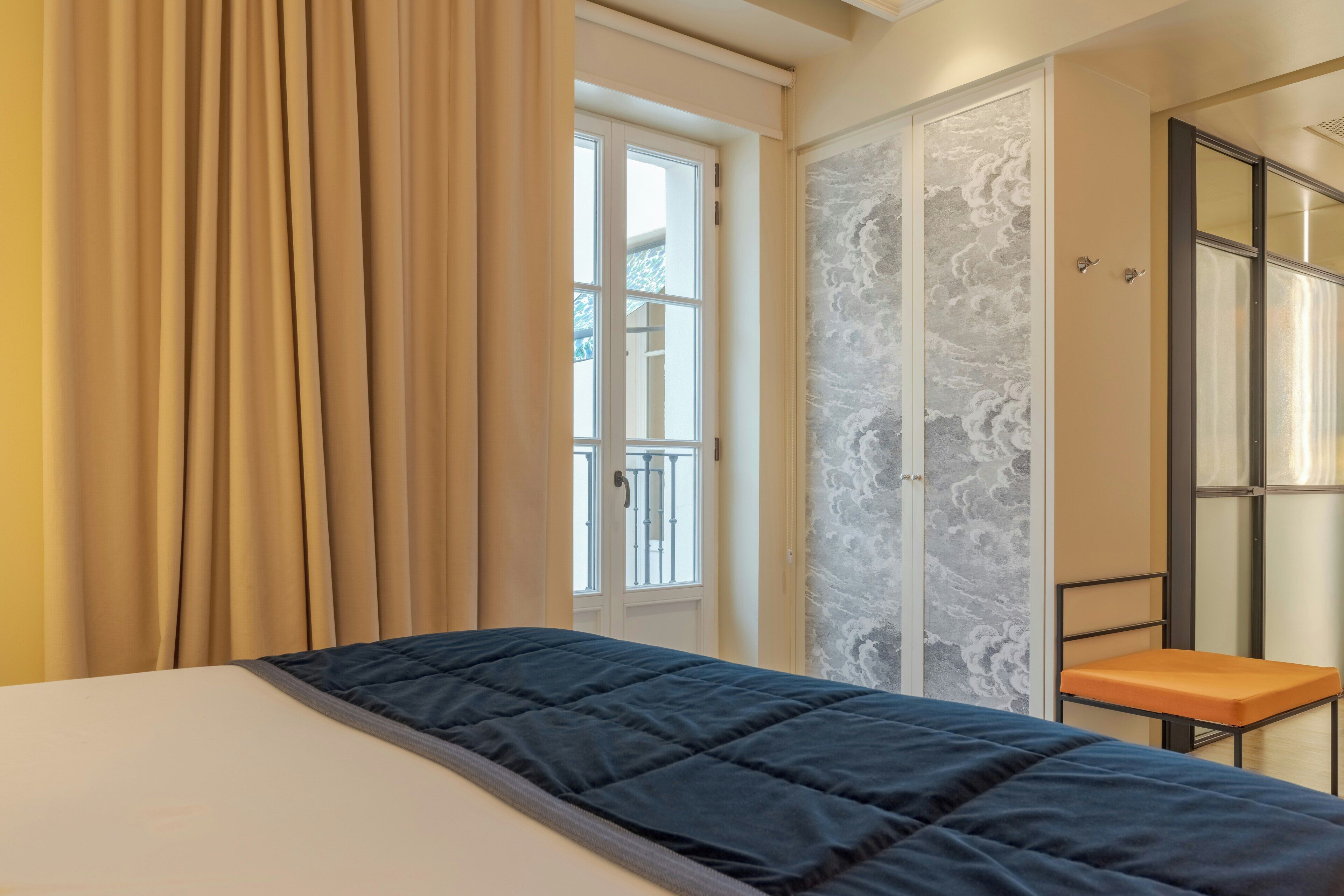 A bedroom with a bed, a window with curtains, a door with a mirror, and a small table.