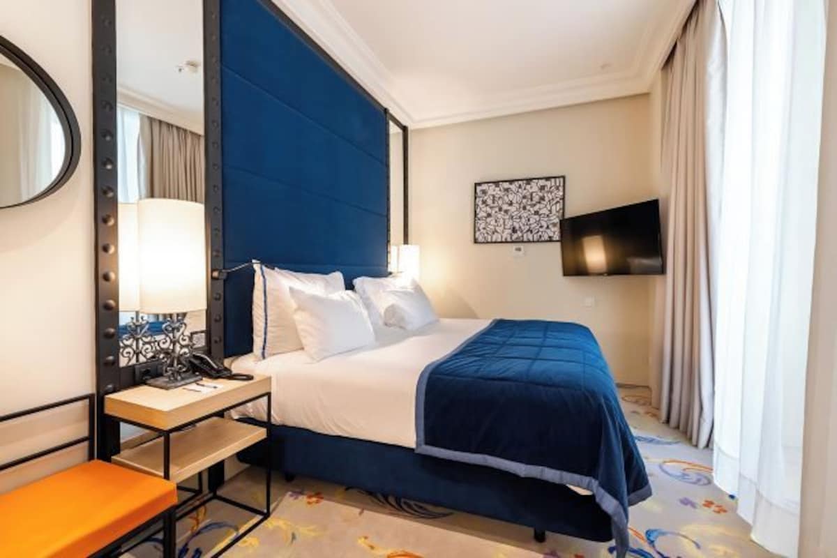 Una camera d'albergo con un letto, un comodino, una lampada e una televisione.