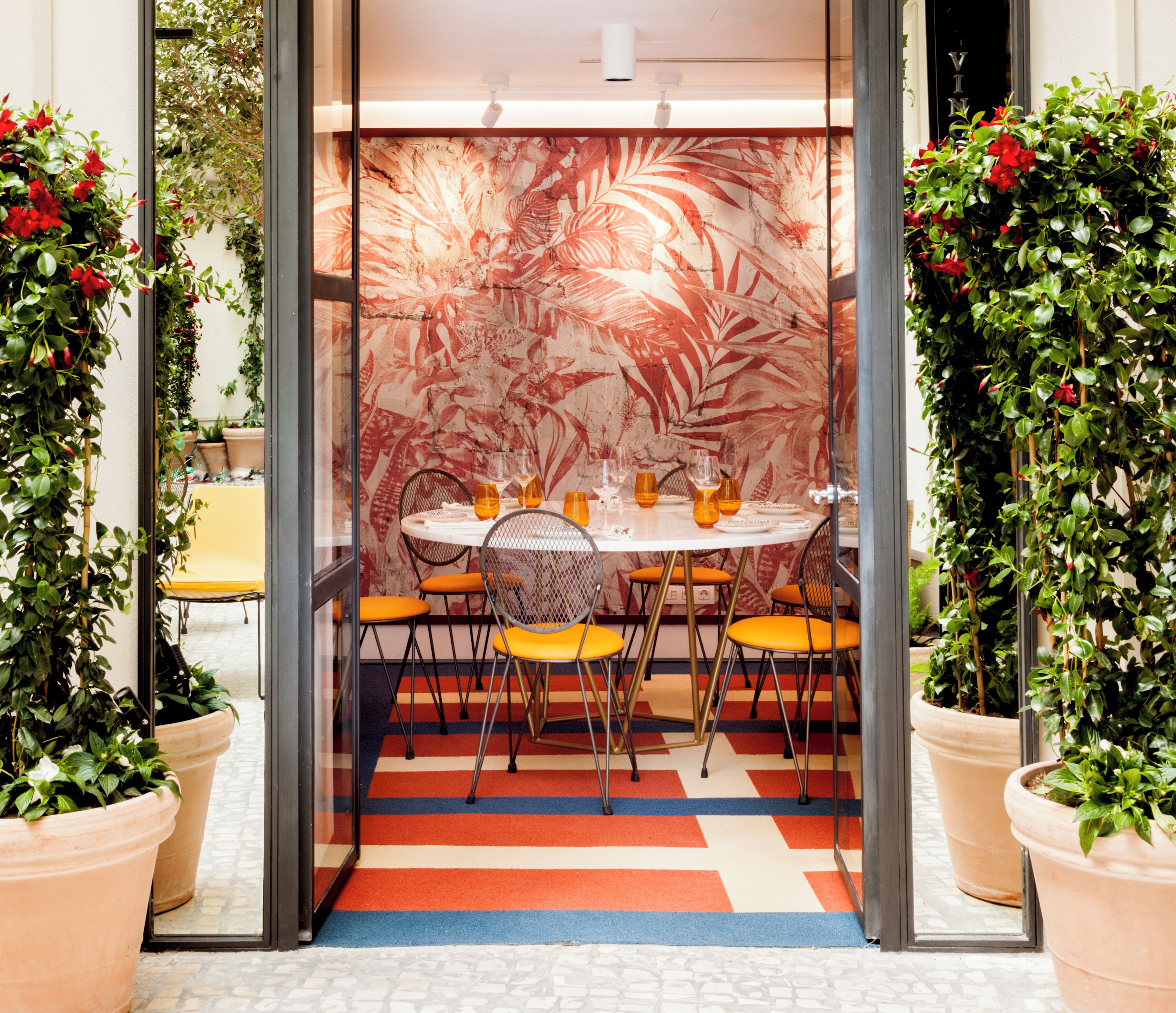 Un comedor con una mesa redonda, sillas color naranja y una pared con estampado.