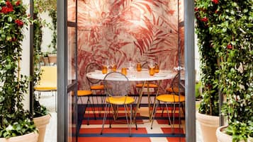 Un comedor con una mesa redonda, sillas color naranja y una pared con estampado.