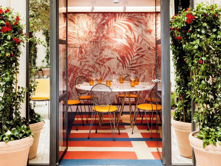 Un comedor con una mesa redonda, sillas color naranja y una pared con estampado.