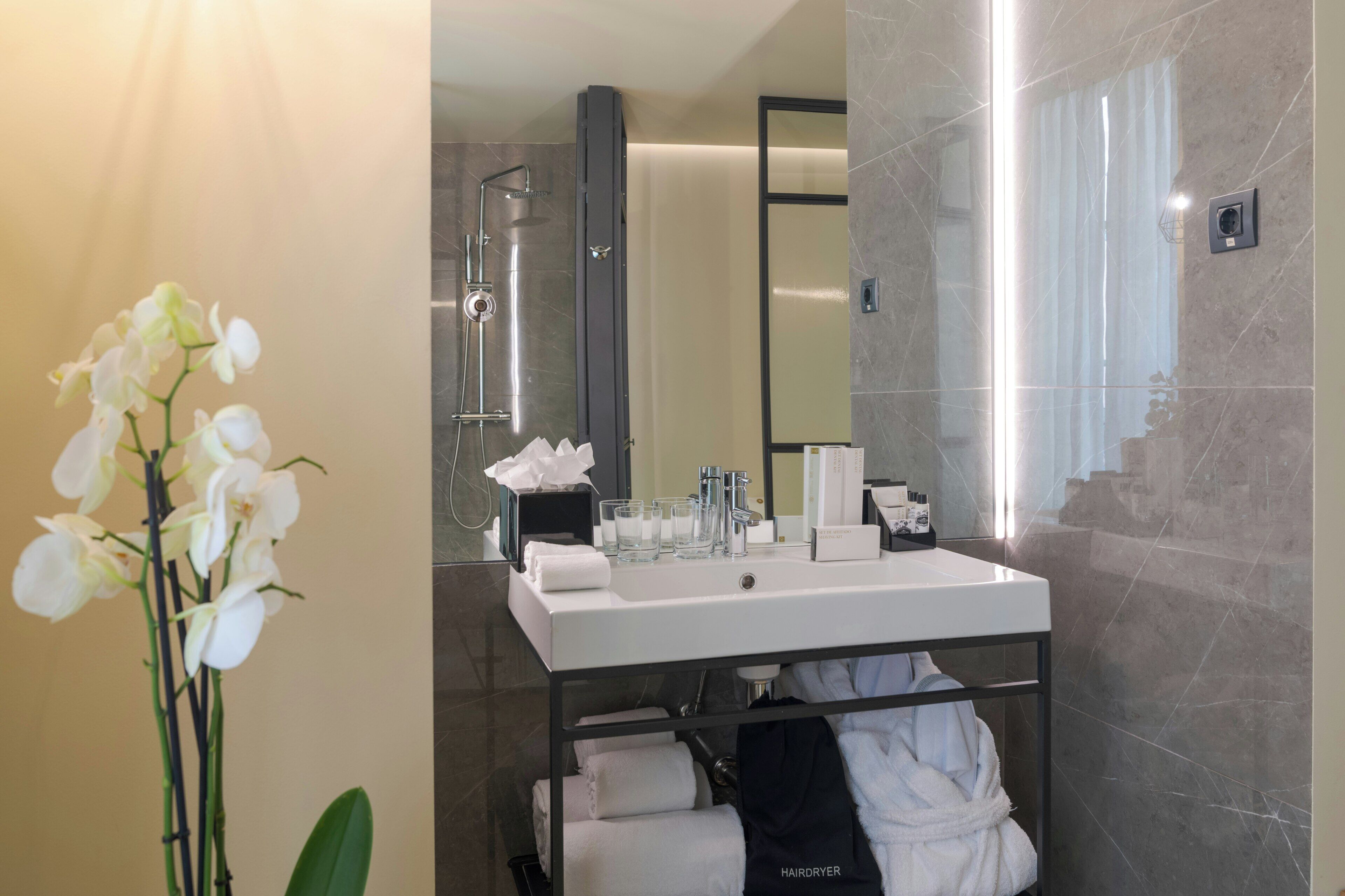 Un bagno moderno con un lavandino bianco, cabina doccia in vetro e uno specchio.