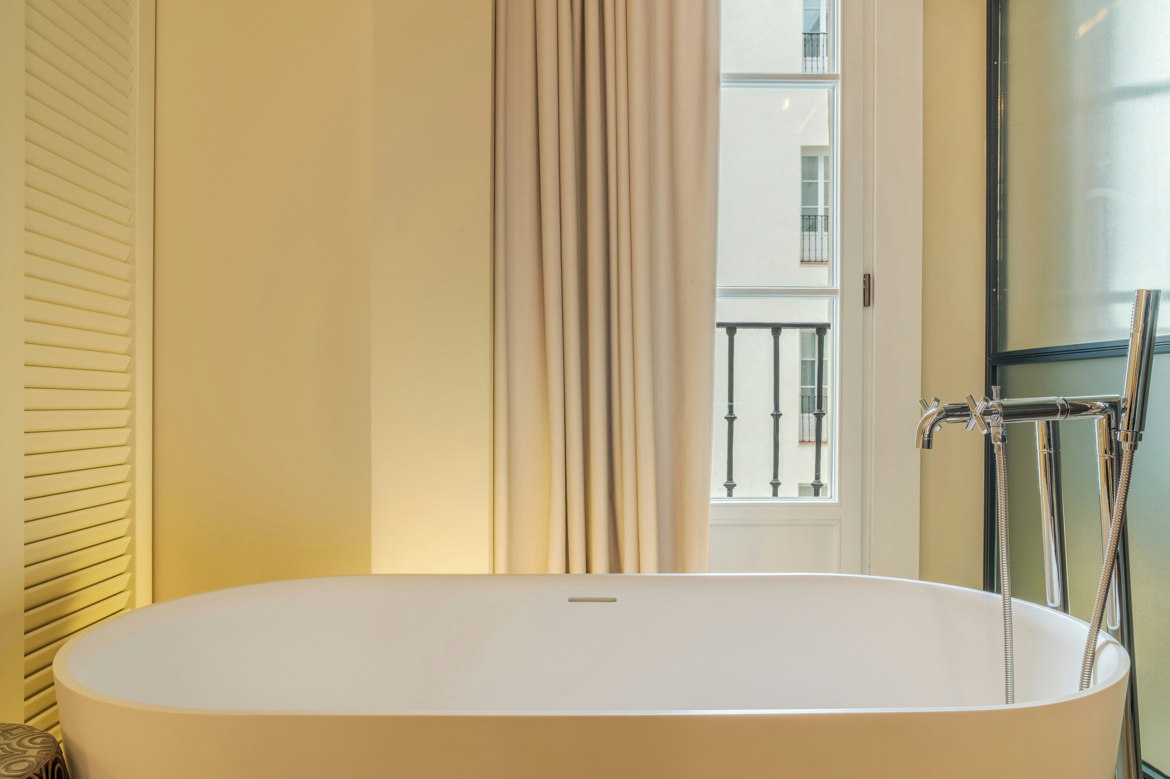 Ein Badezimmer mit einer freistehenden Badewanne, einem Fenster mit Blick auf einen Balkon und einer modernen Duscheinrichtung.
