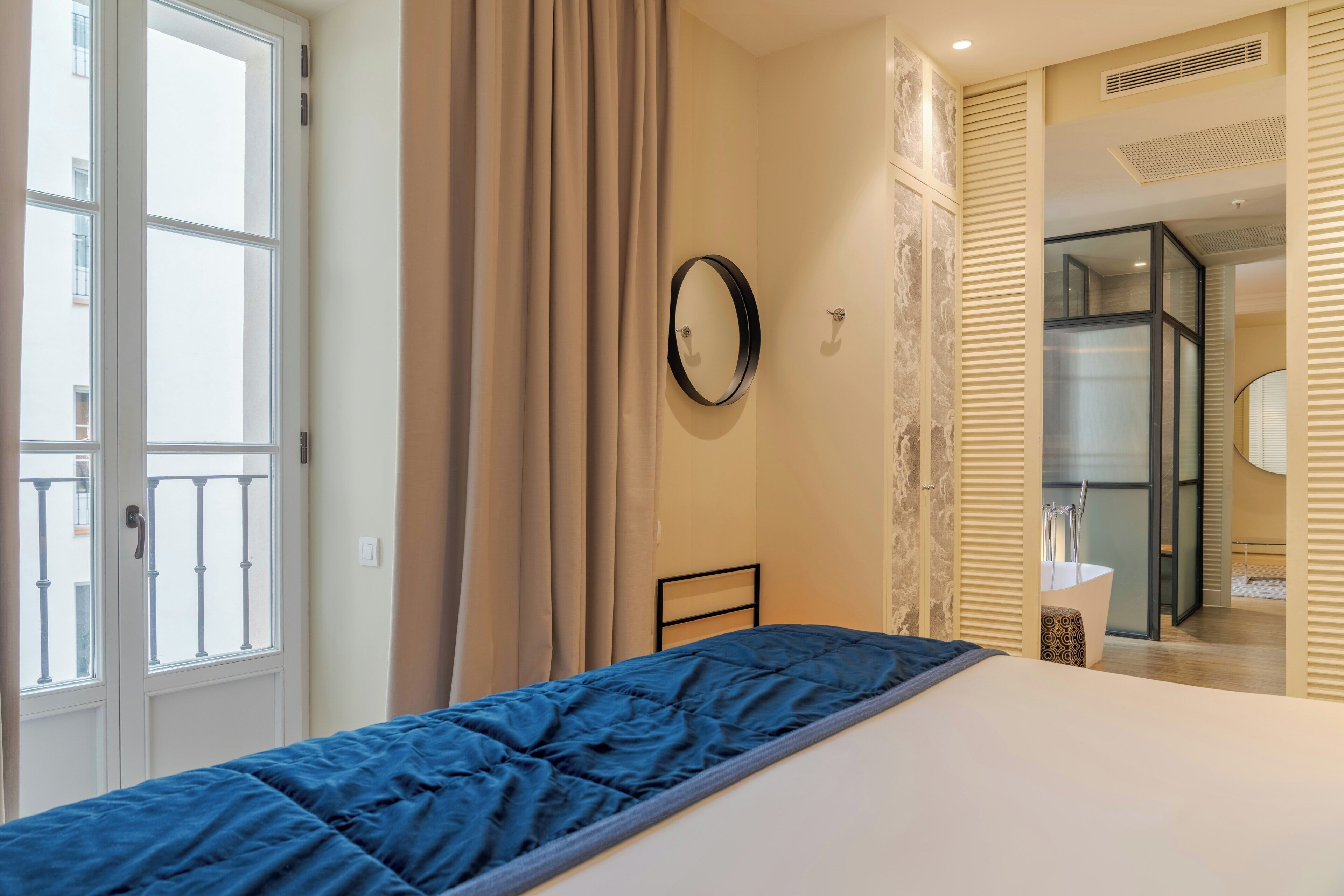 A bedroom with a bed, a window, a door, and a bathroom visible through a sliding door.