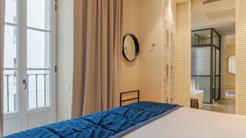 A bedroom with a bed, a window, a door, and a bathroom visible through a sliding door.