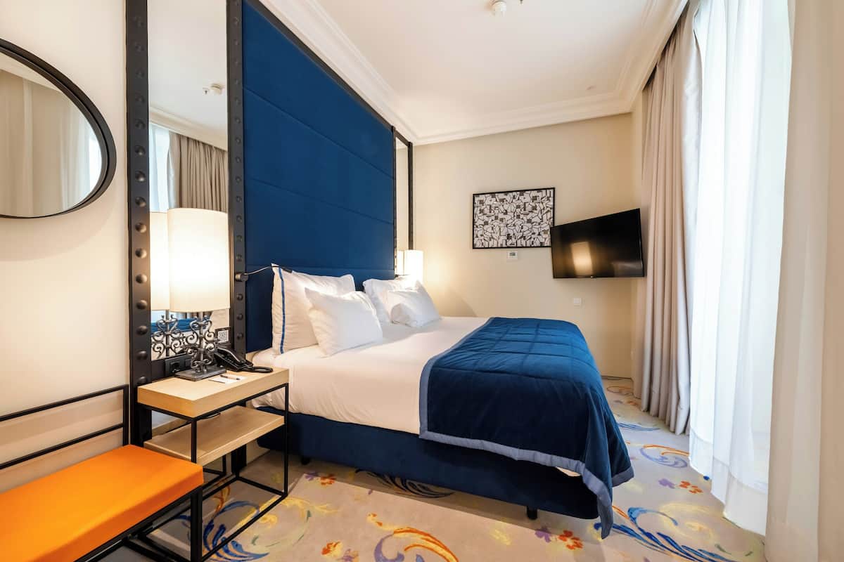 Une chambre d’hôtel avec un lit, une table de chevet, une lampe et un téléviseur fixé au mur.