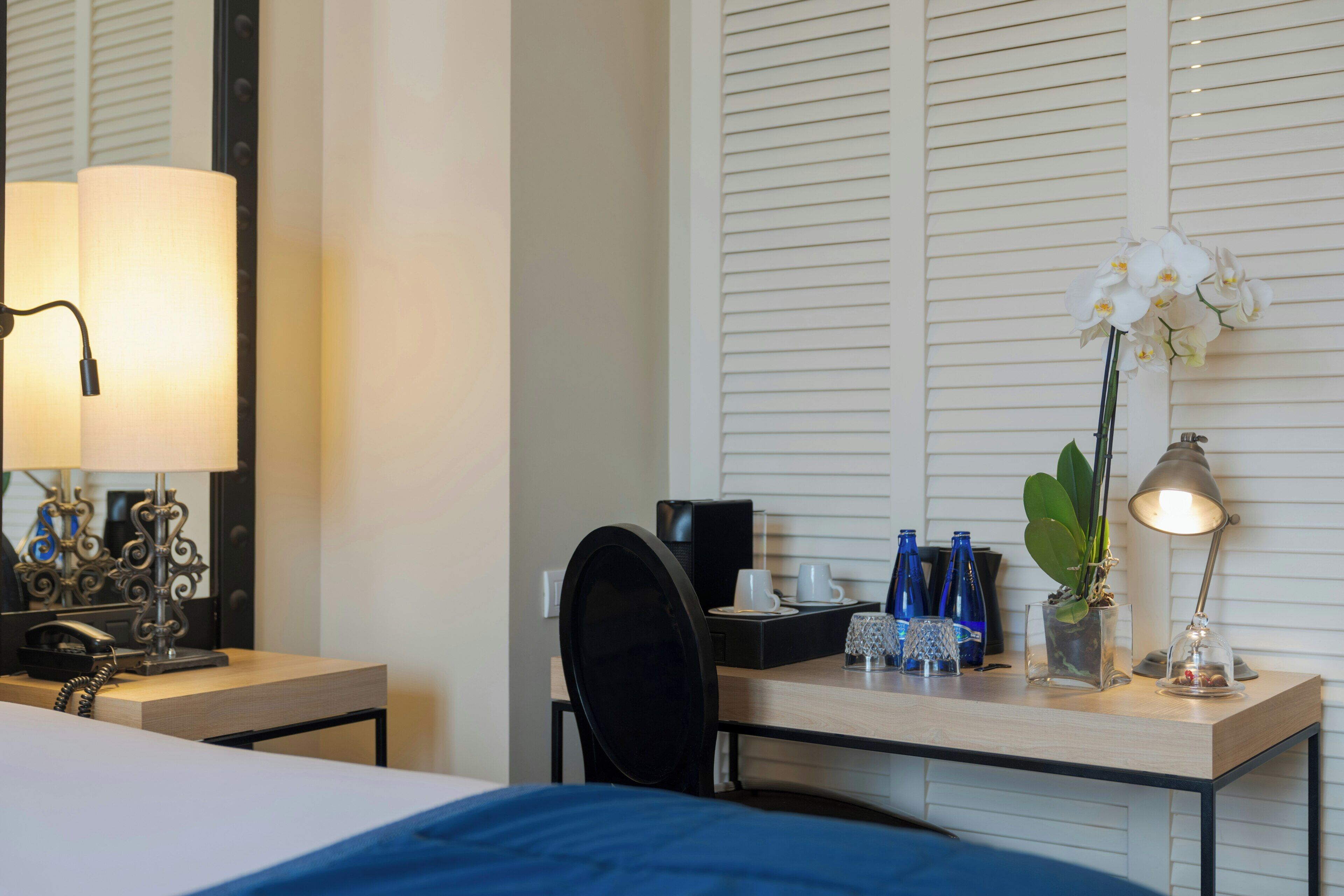 Ein Hotelzimmer mit einem Bett, einem Schreibtisch mit Lampe, einer Kaffeemaschine und einer Vase mit Blumen.