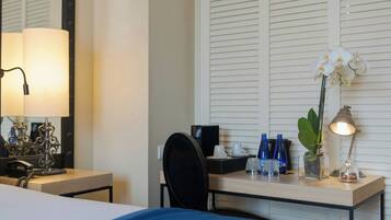 Ein Hotelzimmer mit einem Bett, einem Schreibtisch mit Lampe, einer Kaffeemaschine und einer Vase mit Blumen.