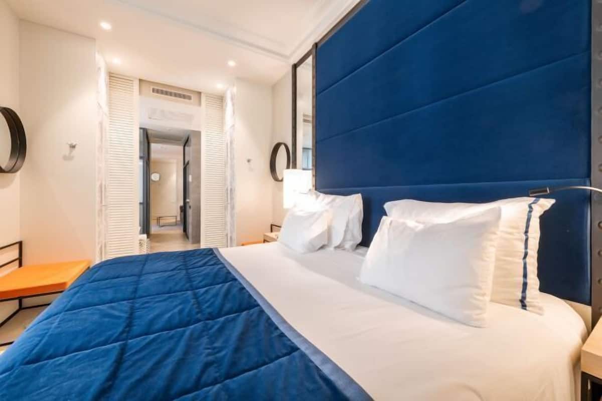 Une chambre d’hôtel comprenant un lit, une table de chevet, un miroir et une porte donnant accès à une salle de bain.