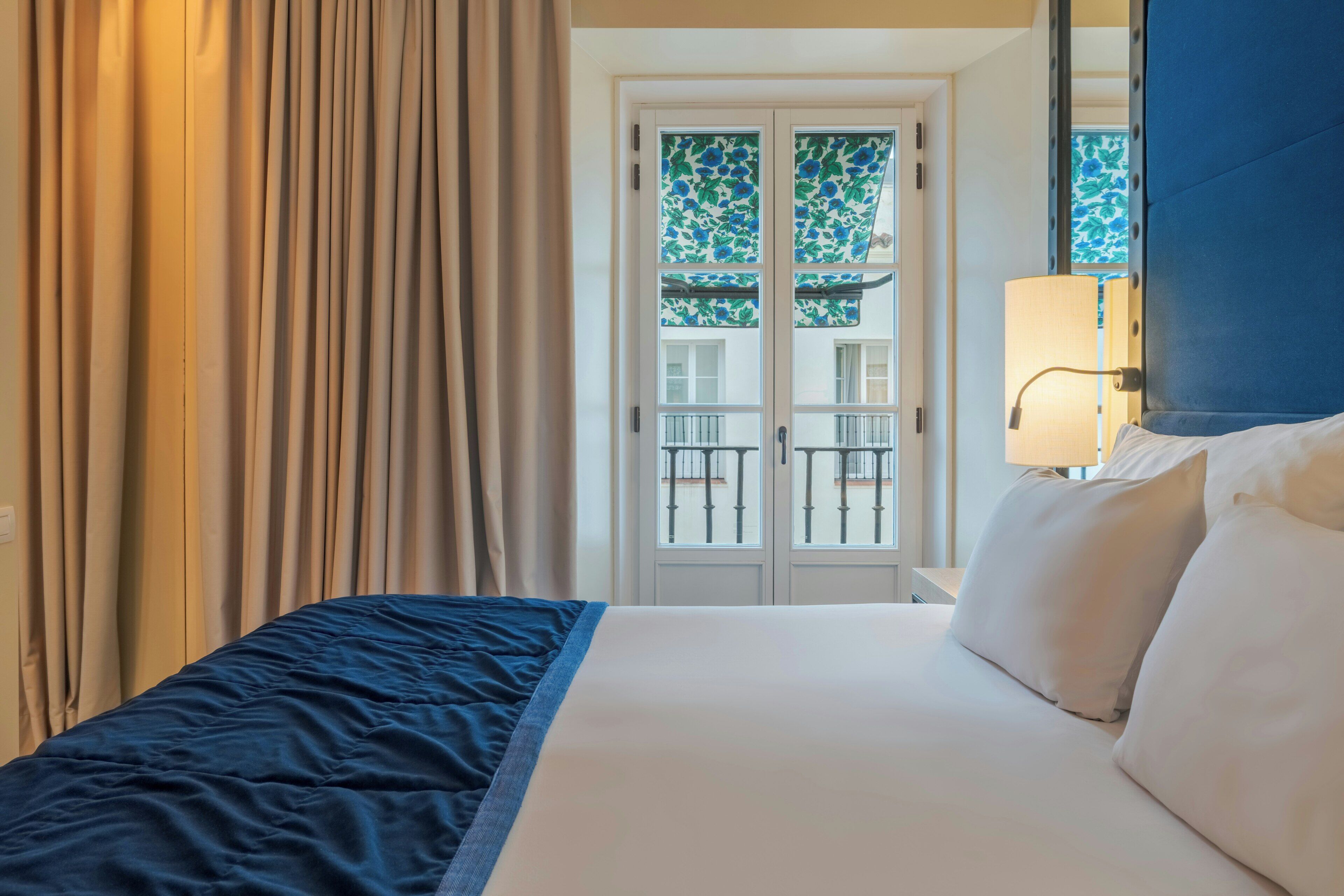 A hotel room with a bed, curtains, a window with a view, and a lamp.