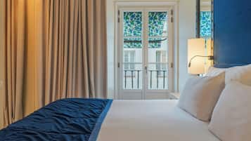 A hotel room with a bed, curtains, a window with a view, and a lamp.