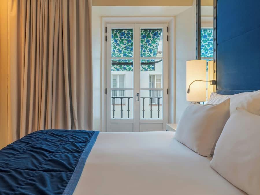A hotel room with a bed, curtains, a window with a view, and a lamp.