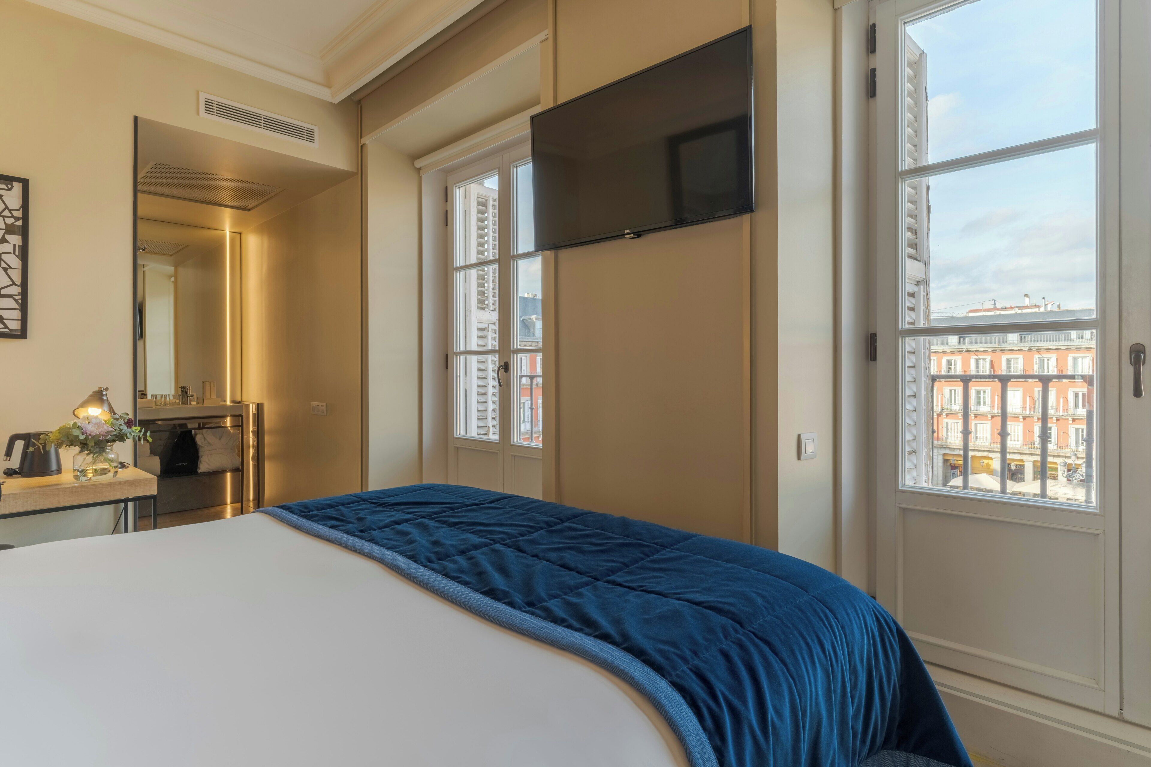 A hotel room with a bed, a flat-screen TV, a desk with a lamp, and a window with a city view.