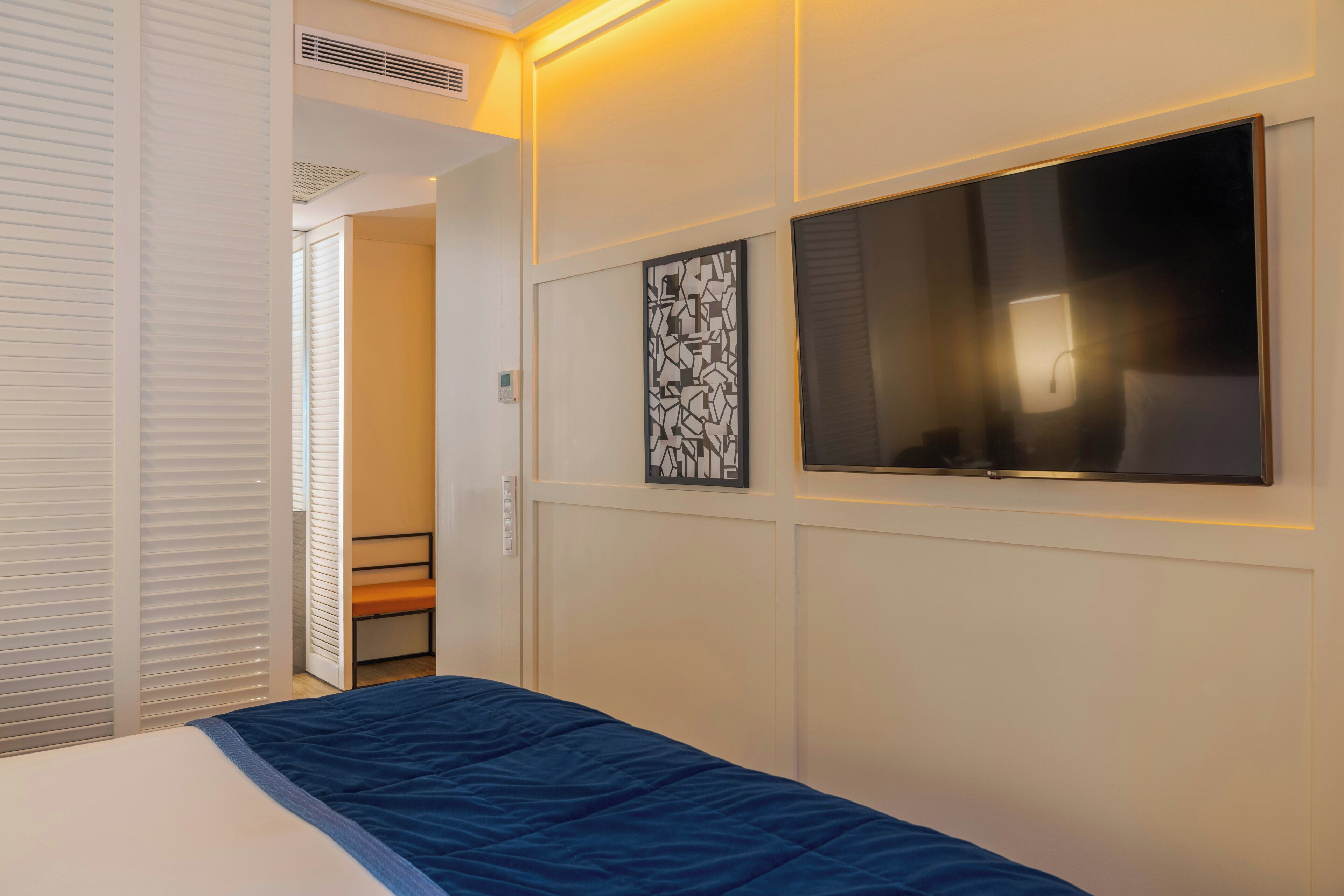 Una habitación de hotel con una cama, televisión montada en la pared, una puerta con picaporte y un ventanal pequeño.