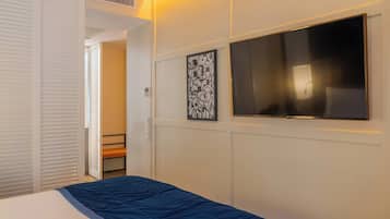 Una habitación de hotel con una cama, televisión montada en la pared, una puerta con picaporte y un ventanal pequeño.