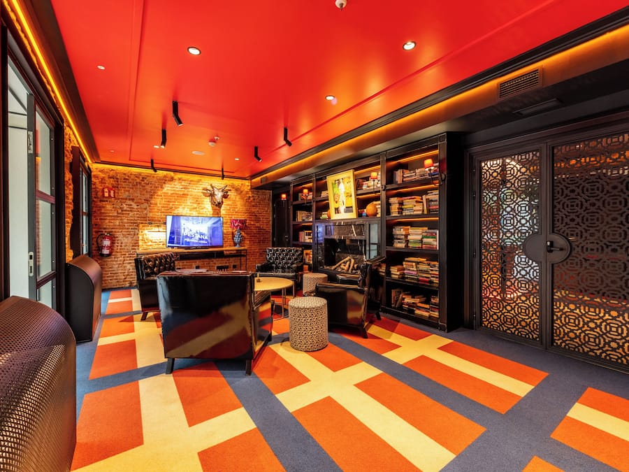 A cozy lounge area with a brick wall, a television, a bookshelf, and a patterned carpet.