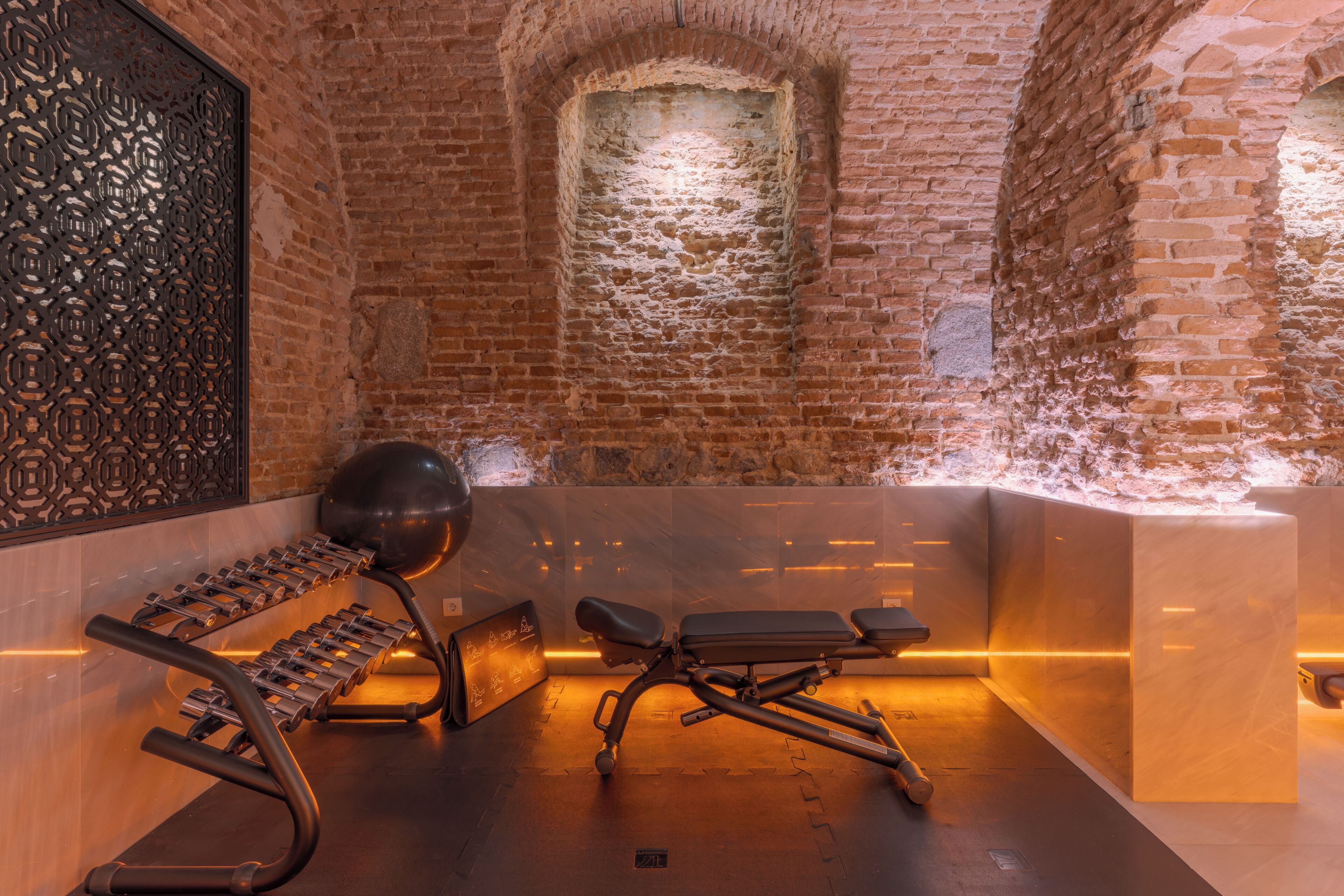 A brick-walled room with a massage table, a massage chair, and a set of weights.