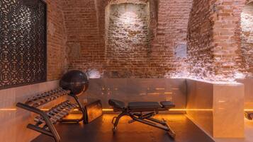 A brick-walled room with a massage table, a massage chair, and a set of weights.
