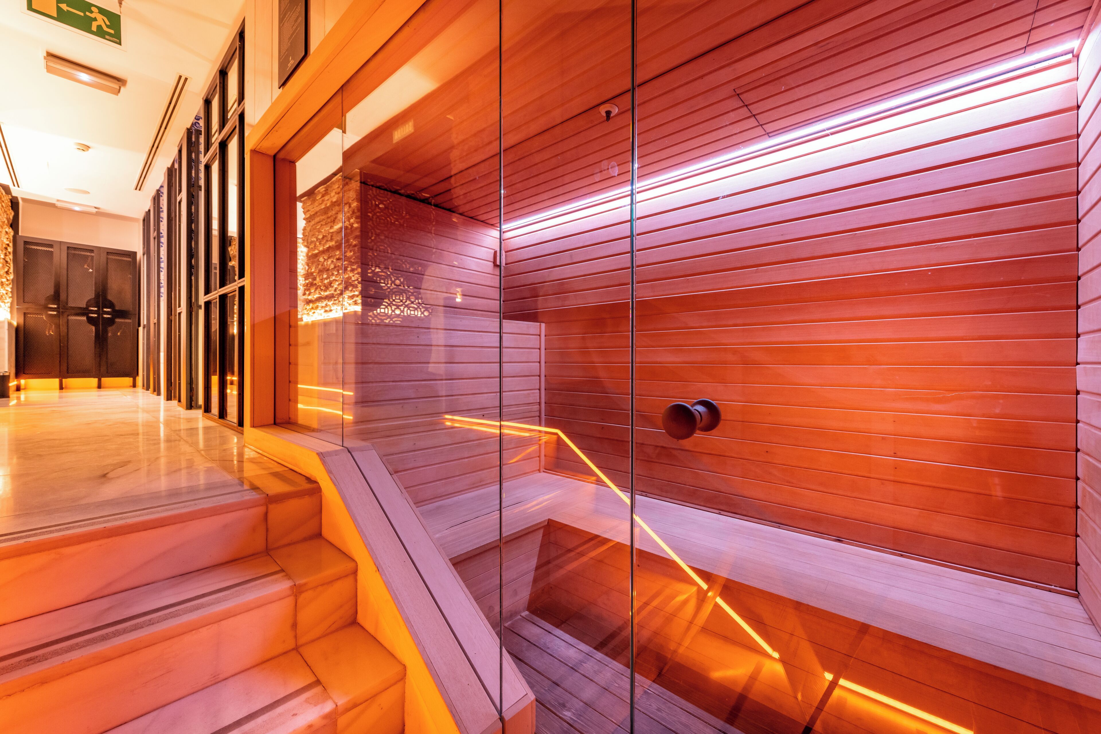Un interno moderno con una scala che conduce a un livello inferiore, una parete divisoria in vetro e un muro di legno con linee orizzontali.