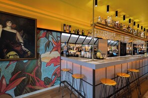 Angolo bar con un murale, sgabelli da bar e scaffali pieni di bottiglie e bicchieri.