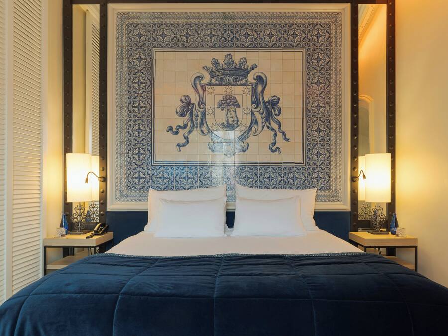 Habitación de hotel con una cama grande, dos lámparas de noche, un tapiz decorativo en la pared y una ventana con persianas.