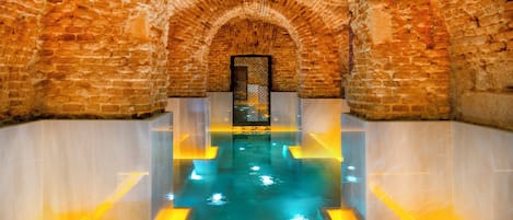 An arched brick interior with a central pool and a patterned door.