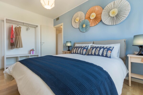 A bedroom with a large bed, a wardrobe, a bedside table with a lamp, and decorative paper fans on the wall.