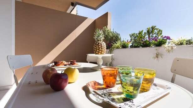 A table with fruits, glasses, and a white chair in a sunny outdoor setting. - Appartamento 5th Floor (Cagliari)