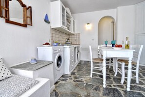 A compact kitchen with a washing machine, a dining table with chairs, and a small seating area with a sofa and cushions. - Private Vacation Home - Near Mykonos New Port (Mykonos)