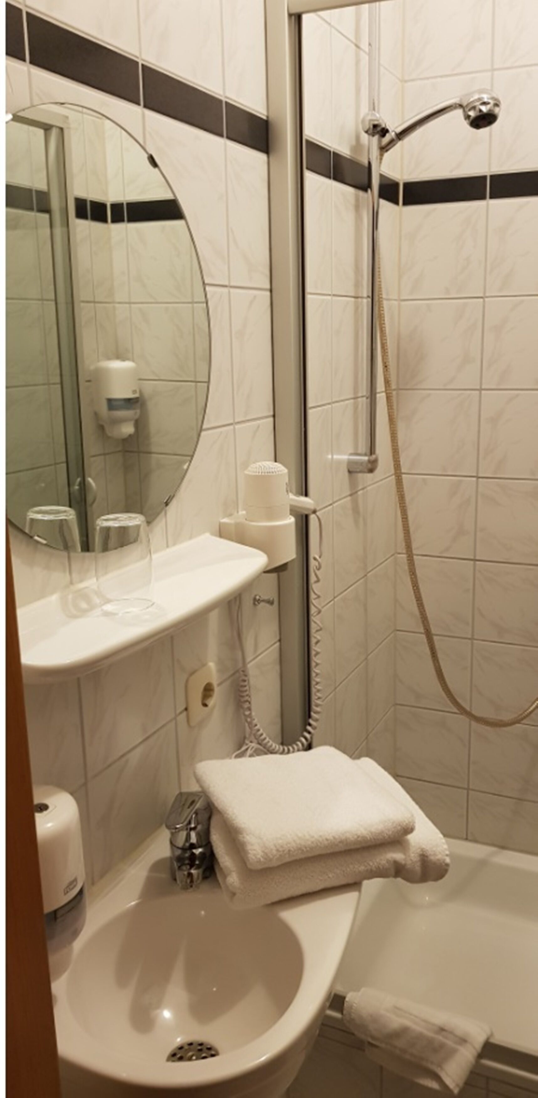 A bathroom with a sink, mirror, towel, shower, and toilet.