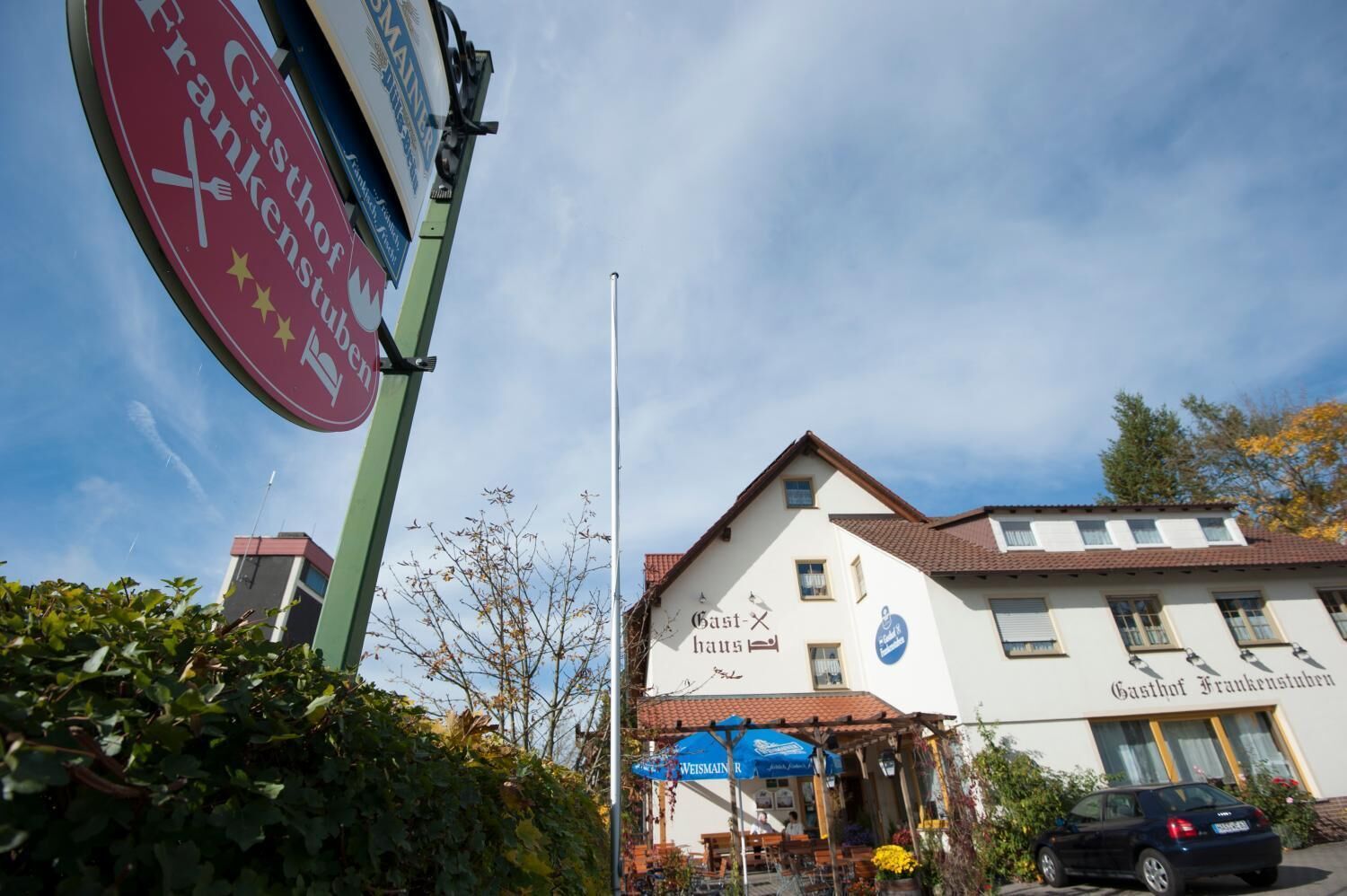 A building with a sign reading "Gasthof Frankenstuben" and a blue umbrella outside.