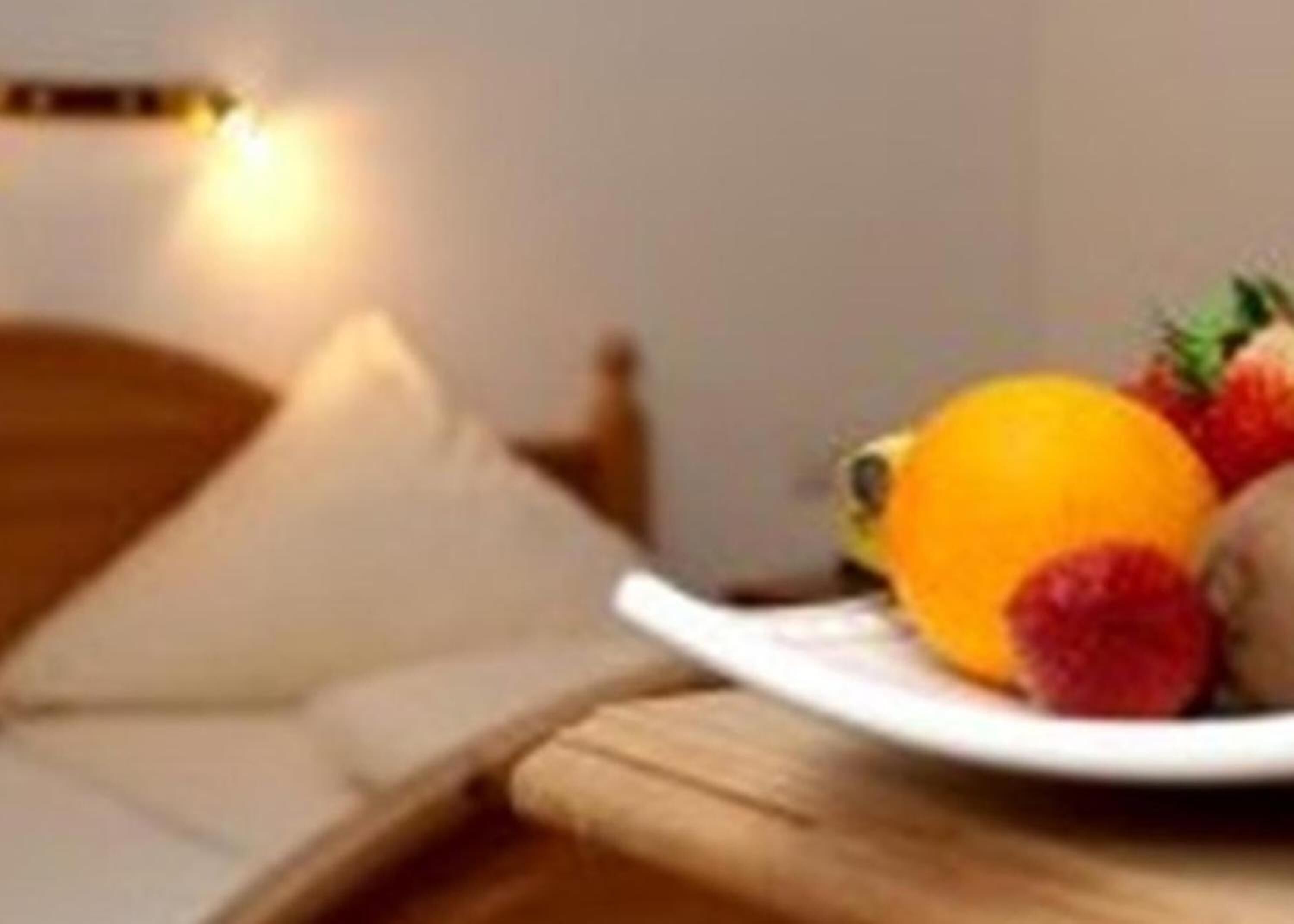 Een bed met een wit kussen en een nachtkastje met een schaal fruit.