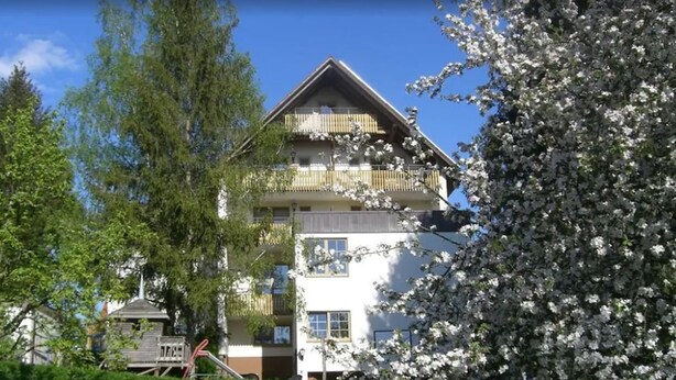 A multi-story building with a balcony on the upper floor, surrounded by trees and blooming flowers. - Gasthof Frankenstuben (Ebern)