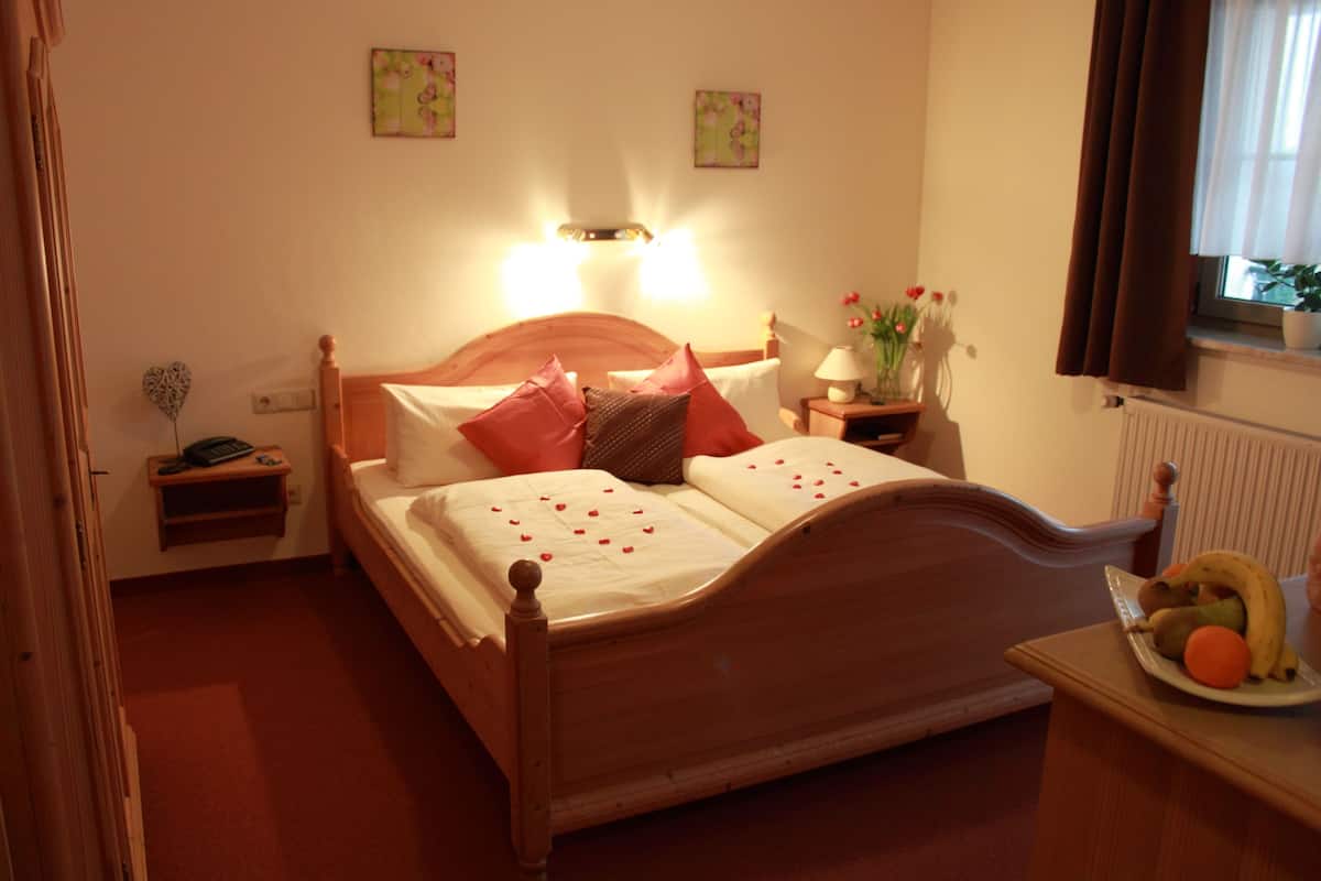 A bedroom with a wooden bed, bedside tables, a nightstand, a lamp, a potted plant, and a window with curtains.