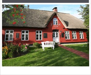 A red building with a thatched roof, a white bench, and a garden with flowers.