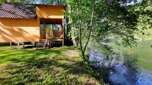 A wooden cabin with a deck overlooking a lake, surrounded by trees. - Riverland (Duga Resa)