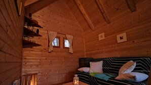 A cozy cabin room with a wooden interior, a bed with striped bedding, a small table with a lantern, and a window with curtains. - Riverland (Duga Resa)
