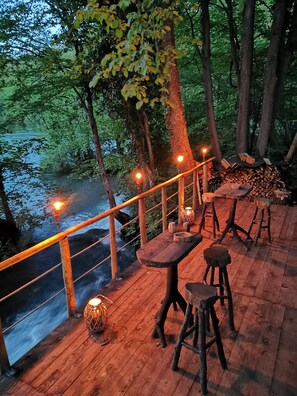 A wooden deck with tables and stools overlooking a river, surrounded by trees. - Riverland (Duga Resa)