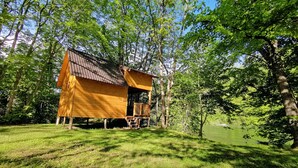 A wooden cabin with a sloped roof, surrounded by lush greenery and a pond. - Riverland (Duga Resa)