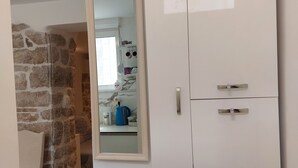 Ein Zimmer mit einem weißen Wandschrank, einem Spiegel, der eine Küchenzeile reflektiert, und einer Steinwand.