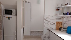 Eine Küche mit Mikrowelle, Kühlschrank, Marmor-Spritzschutz und einem blauen Behälter auf der Arbeitsfläche.