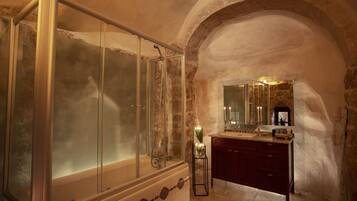 A bathroom with a glass-enclosed shower, a vanity with a mirror, and a stone archway.