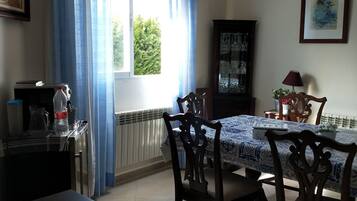 Un comedor con una mesa dispuesta para cuatro, un armario con cristalería y una ventana con cortinas.
