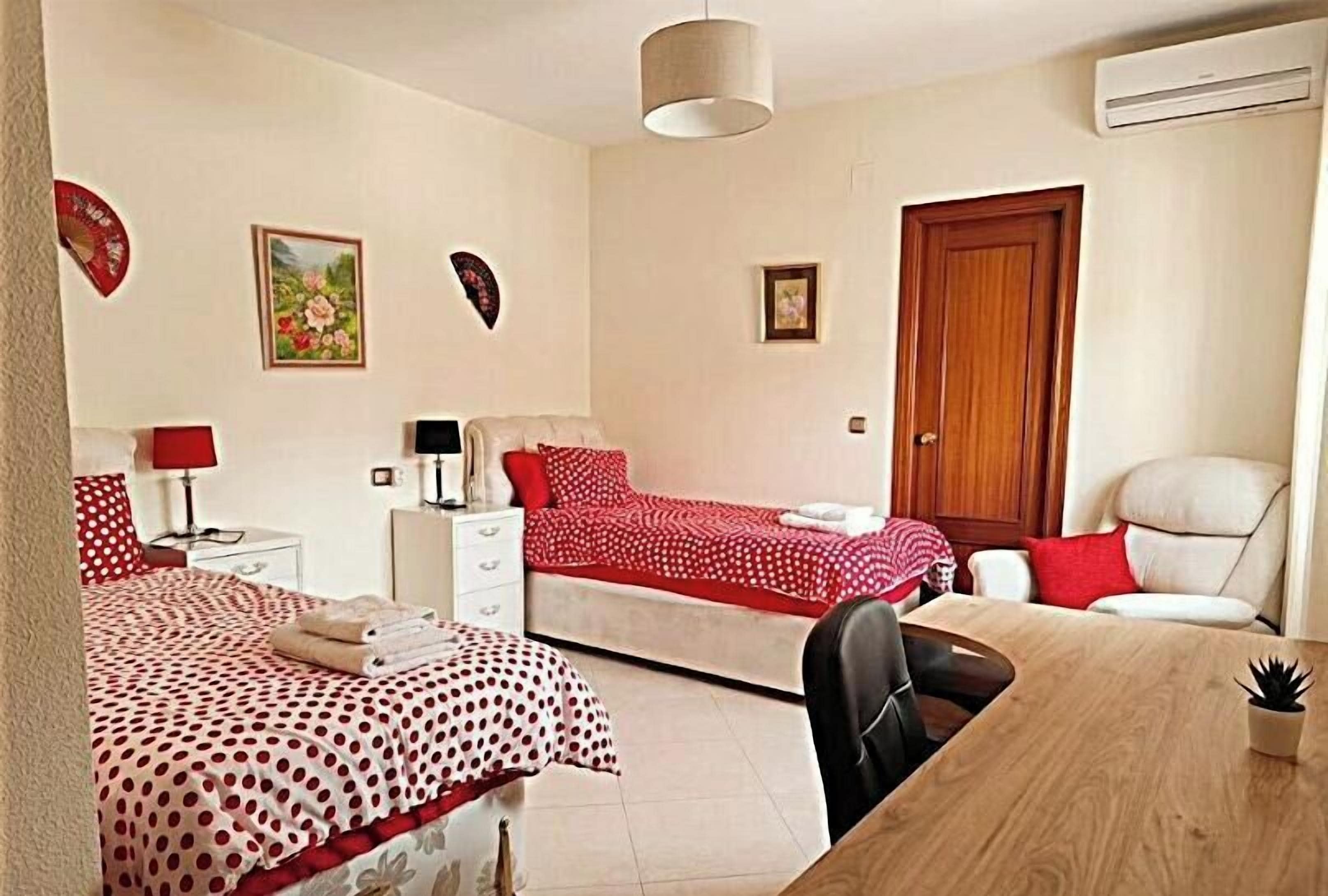 A room with two beds, a desk, a chair, a lamp, and a door.